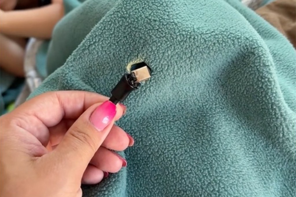 A woman holds a burnt USB-C charging cable that had been lying on a blanket in her home